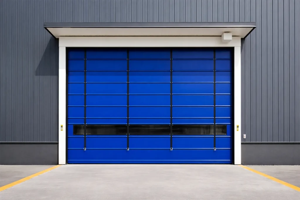 Blue exterior PVC fold-up door integrated into a corrugated metal building facade, providing reliable weather protection and rapid access for logistics hubs.