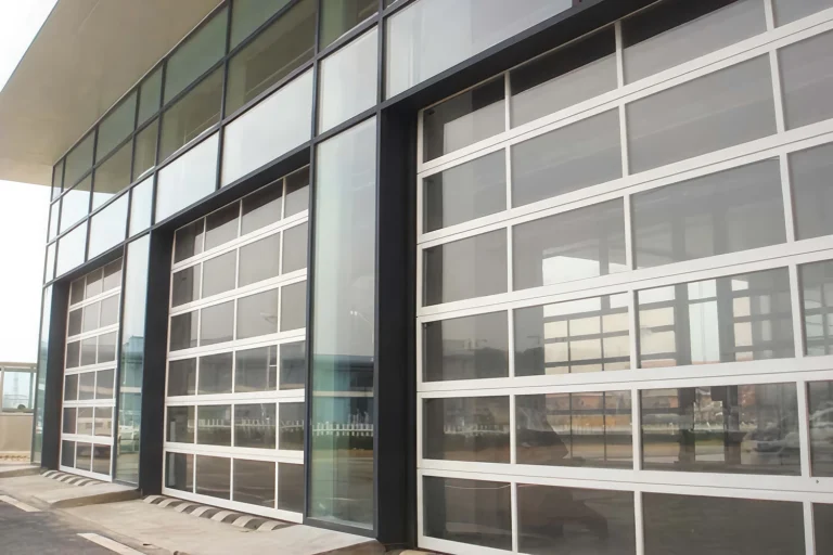 Exterior view of a modern commercial facade featuring heavy-duty aluminum full-view garage doors with clear glass panels, manufactured by ABX to maximize natural lighting and architectural aesthetics.