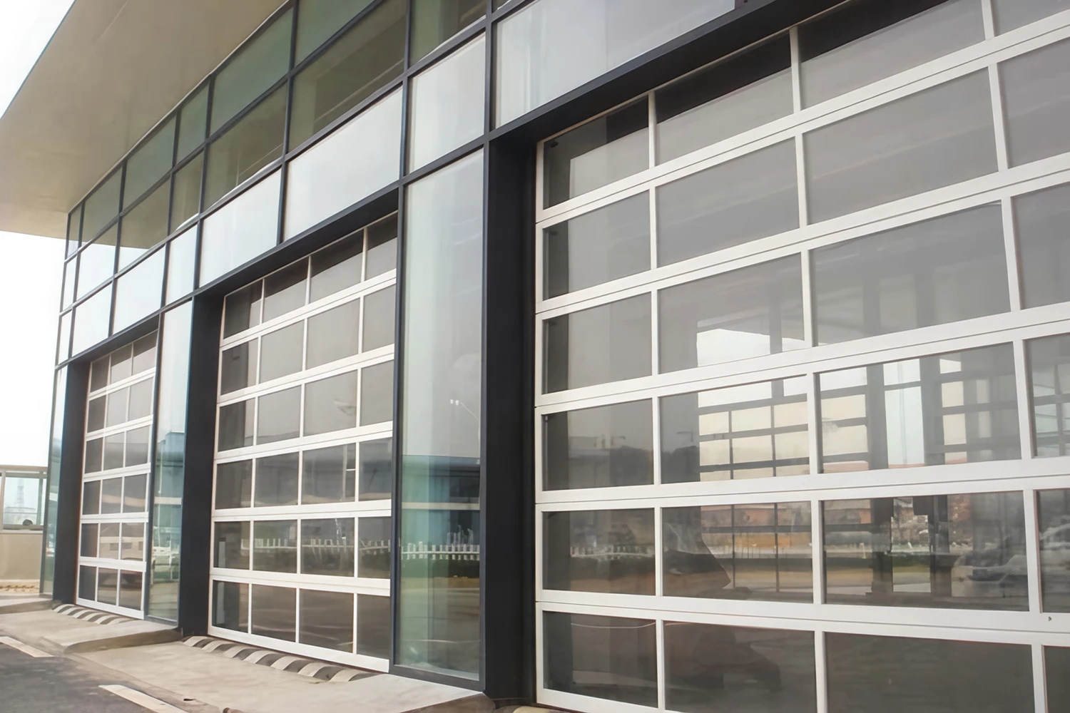 Exterior view of a modern commercial facade featuring heavy-duty aluminum full-view garage doors with clear glass panels, manufactured by ABX to maximize natural lighting and architectural aesthetics.