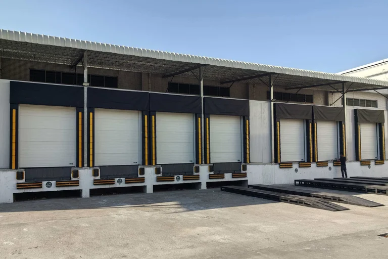Exterior view of a modern logistics center featuring a row of commercial dock high doors integrated with heavy-duty dock seals and levelers. ABX OEM manufacturer provides CE/ISO certified loading bay integration solutions for global wholesale projects.