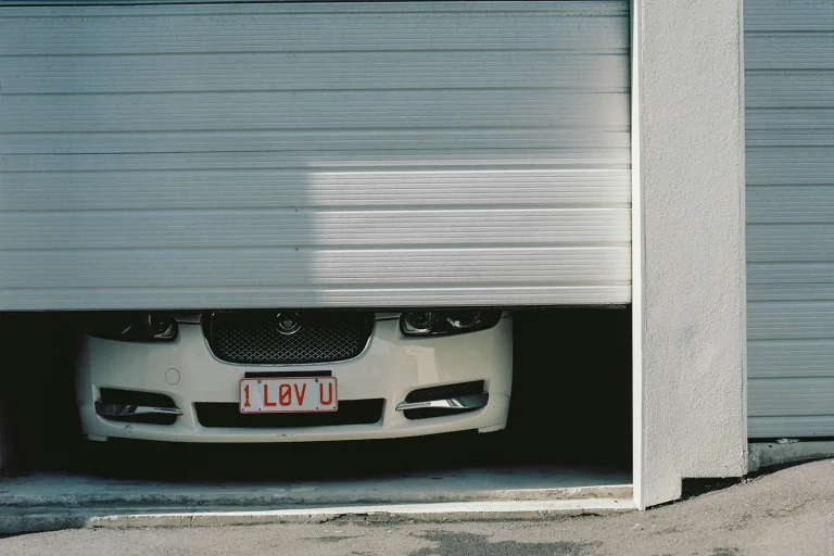 A vehicle positioned under a commercial sectional door, illustrating the high risk of bottom panel impacts. ABX offers OEM commercial garage door bottom section replacements and auto-recovery upgrades to restore structural integrity.