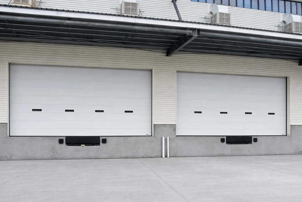 Two white commercial overhead sectional doors with vision panels on the exterior of a modern logistics warehouse