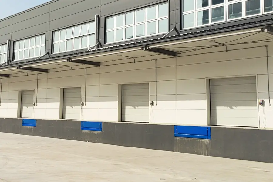 Row of grey commercial sectional doors at a loading dock with blue dock levelers.