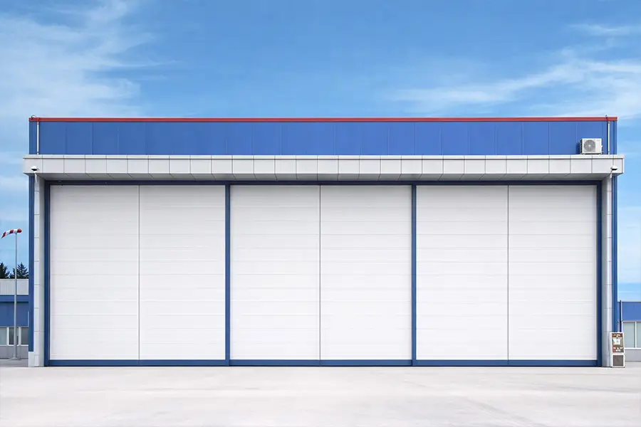 Extra large white sliding aircraft hangar doors installed on a modern blue aviation facility by ABX Doors.