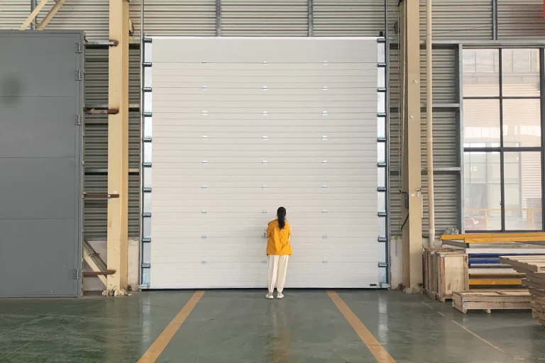 A person standing in front of a massive heavy-duty oversized commercial garage door, demonstrating the impressive 15ft to 18ft scale engineered by ABX for industrial facilities and heavy machinery access.