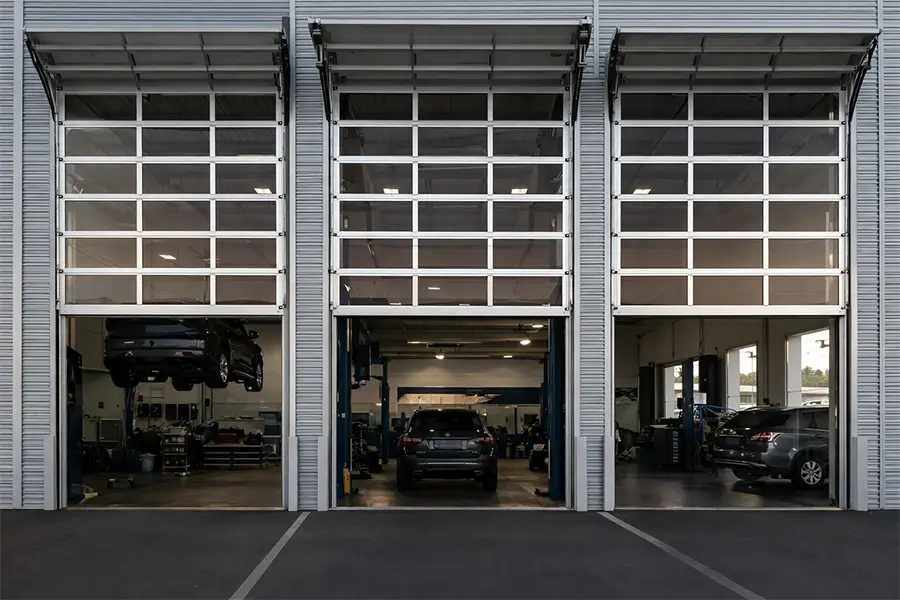 Exterior view of high-lift full view sectional doors at a modern automotive service center, allowing maximum clearance for car lifts.