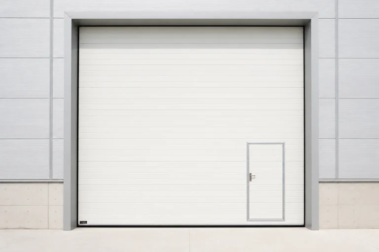 Blue industrial polyurethane insulated sectional door in a modern cold storage facility with conveyor rollers, stainless steel control panels, and clean white walls.