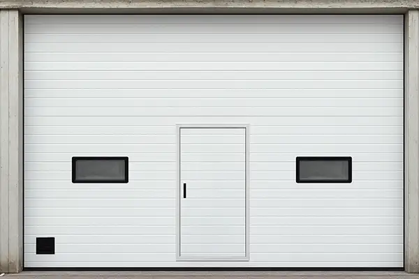 White industrial sectional door featuring a pedestrian wicket door and vision windows for easy access.