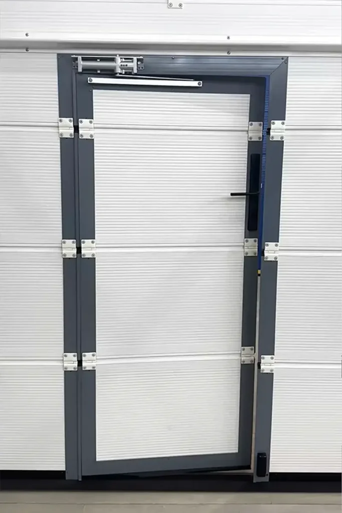 Close-up of a built-in wicket door on modern garage doors, featuring heavy-duty hinges and a door closer for secure pedestrian access
