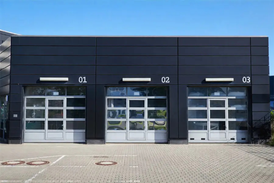 Row of modern grey full-view aluminum garage doors with clear glass panels for industrial buildings.