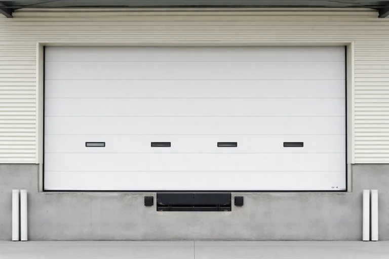 White modern industrial sectional garage door featuring rectangular vision panels installed at a commercial loading dock