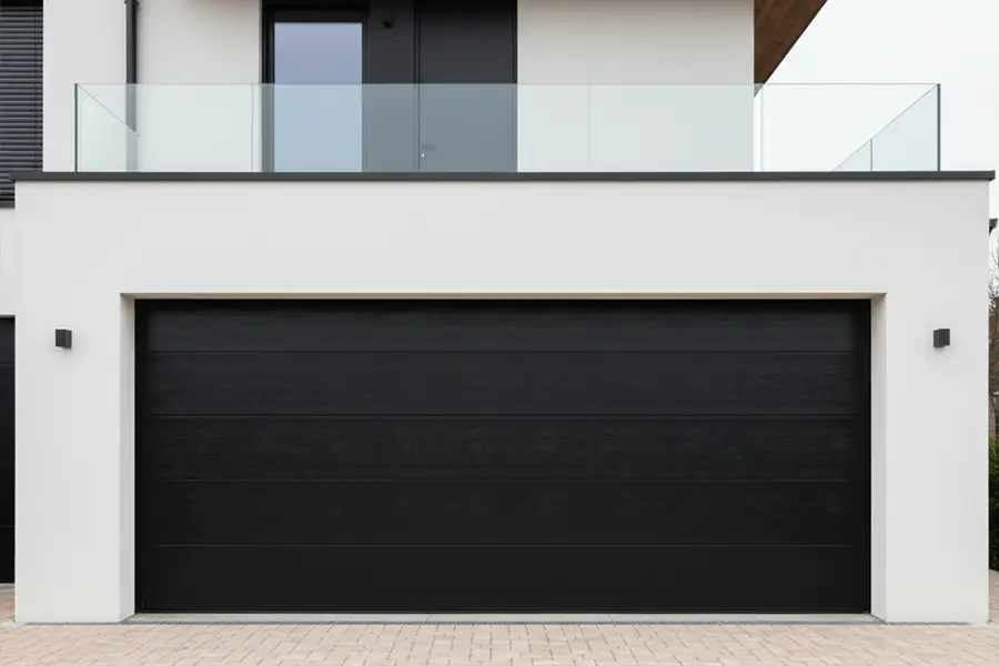 Sleek modern sectional garage door with a flush panel design located beneath a minimalist glass balcony.