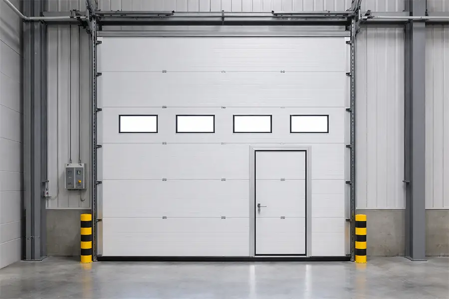 White industrial sectional door featuring four vision panels and an integrated pedestrian wicket door for efficient personnel access.